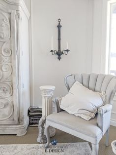 a white chair sitting in front of a window next to a lamp and a mirror