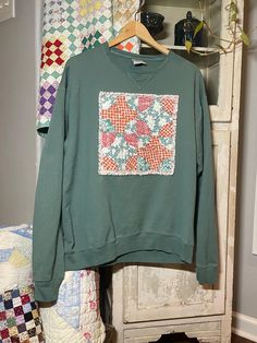 a green sweatshirt with an orange and white patchwork design on the front hanging from a clothes rack