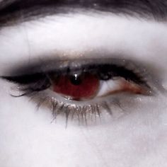 the eye of a woman with long lashes and red eyeshade is seen in this close up photo