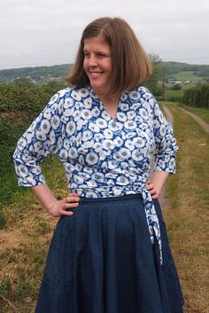 a woman in a blue and white dress standing on a dirt road