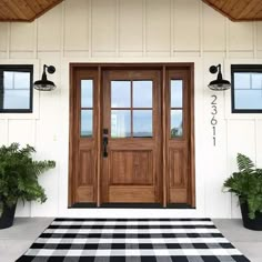 a black and white checkered rug in front of a wooden door with two planters