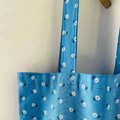 a blue tote bag with white daisies on it hanging from a wooden hook