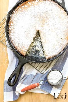 a cake in a skillet with powdered sugar on top and a spoon next to it