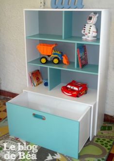 a blue and white book shelf with toy cars on the top, next to a bed