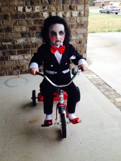 a young child dressed as the joker riding a tricycle in front of a brick wall