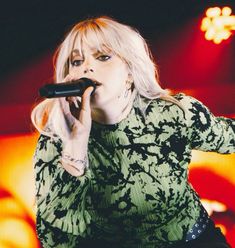 a woman with blonde hair is holding a microphone in her right hand and performing on stage