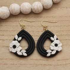 a pair of black and white flower earrings sitting on top of a wooden table next to beads