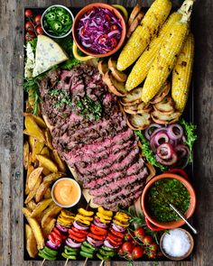 steak, corn on the cob, french fries, and other foods are arranged on a platter