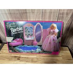 the barbie doll is in its pink box and has a vanity with mirror, sink, and footstool