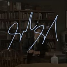 a man sitting in front of a bookshelf with writing on the wall behind him