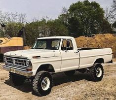 an old white truck is parked in the dirt near some trees and other construction equipment