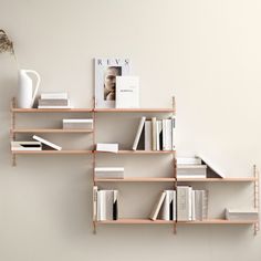 a shelf with books, magazines and a vase on it next to a white wall