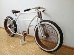 a white bicycle with brown spokes parked against a wall