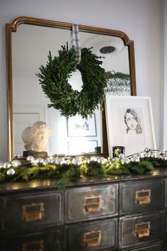 a christmas wreath is on top of an old dresser with greenery and lights around it