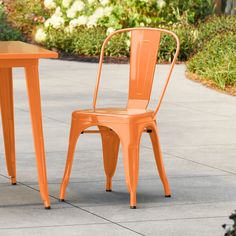 two orange metal chairs sitting next to each other near a table and chair on the sidewalk