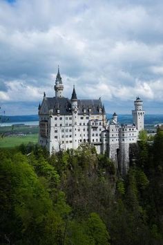 a large white castle sitting on top of a lush green forest next to tall trees