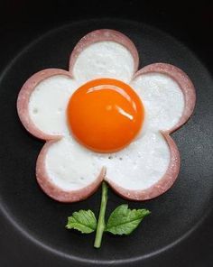 a black plate with an egg, sausage and flower on it's side in the shape of a flower