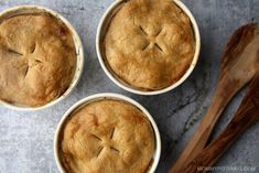 three pies with faces drawn on them sitting in bowls next to an empty wooden spoon