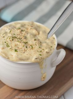 a spoon in a white bowl filled with cheese sauce on top of a wooden cutting board