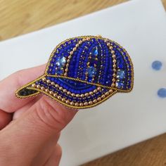 a hand holding a blue beaded ring on top of a wooden table next to a piece of paper