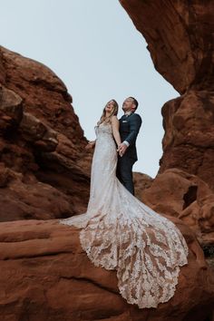 a bride and groom standing on top of a rock formation in front of some rocks