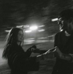 black and white photograph of two people standing next to each other in the street at night