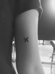 a black and white photo of a person's arm with a small airplane tattoo on it