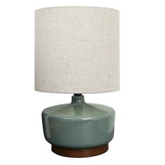 a green table lamp with a white linen shade on the top and wooden base, against a white background