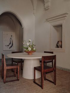 a white table with two wooden chairs and a potted plant sitting on top of it