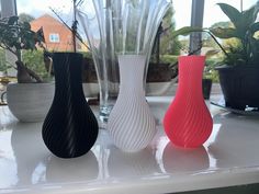 three vases sitting on top of a white counter next to plants and potted plants