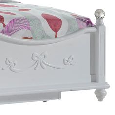 a white bed with pink and green bedspread on it's headboard