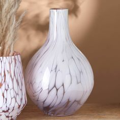 two white vases sitting next to each other on top of a wooden table in front of a brown wall