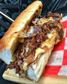 a sandwich with meat and cheese on a cutting board next to an open fire pit