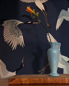 a blue vase sitting on top of a wooden table next to a bird wallpaper