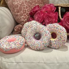 three doughnuts with sprinkles and pink roses on a white couch