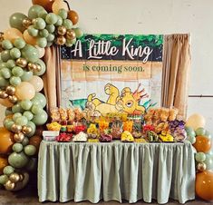 a table topped with lots of food and balloons in front of a sign that says a little king is coming soon