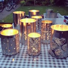 some tin cans are sitting on a checkered table cloth with lights in them and one is lit up