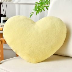 a yellow heart shaped pillow sitting on top of a white couch next to a green plant