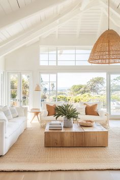 a living room filled with white furniture and large windows overlooking the ocean on a sunny day