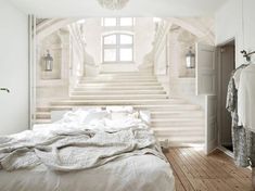 a white bed sitting under a window next to a stair case in front of a doorway