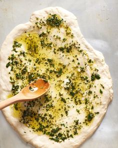 a wooden spoon sitting on top of a pizza crust covered in cheese and pesto