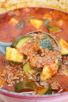 a spoon full of stew with zucchini and bread in the backround