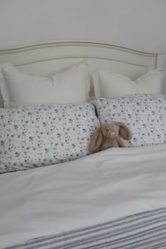 a teddy bear sitting on top of a bed with white sheets and blue striped pillows