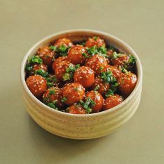 a small bowl filled with meatballs covered in green garnish on top of a table