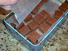 someone is cutting up some chocolate squares on a sheet of wax paper in a pan