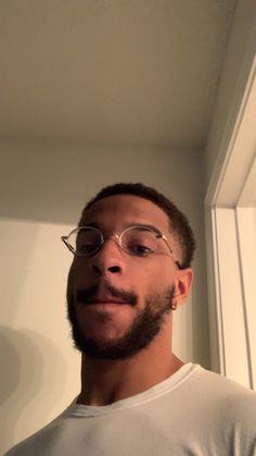 a man with glasses and a beard standing in front of a window looking at the camera