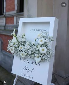 a wedding sign with flowers on it in front of a building