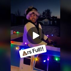 a man wearing a santa hat standing in front of a boat with lights on it