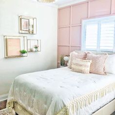 a bedroom with pink walls and white bedding, framed pictures above the headboard