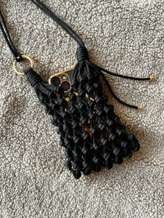 a cell phone case is made out of black and gold braided fabric with an owl charm hanging from it